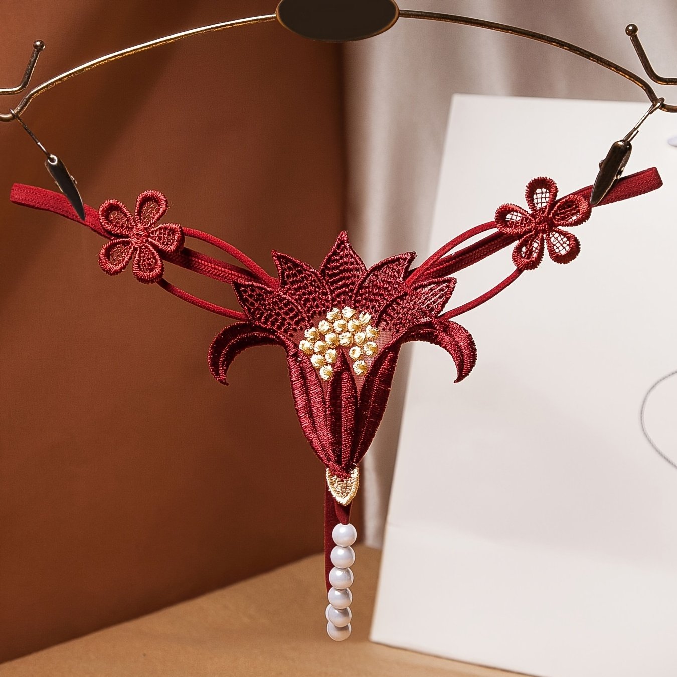 Красный кружевной корсет с перловыми деталями и соответствующим низким стрингом, украшенным цветами крючком и бисерными элементами.