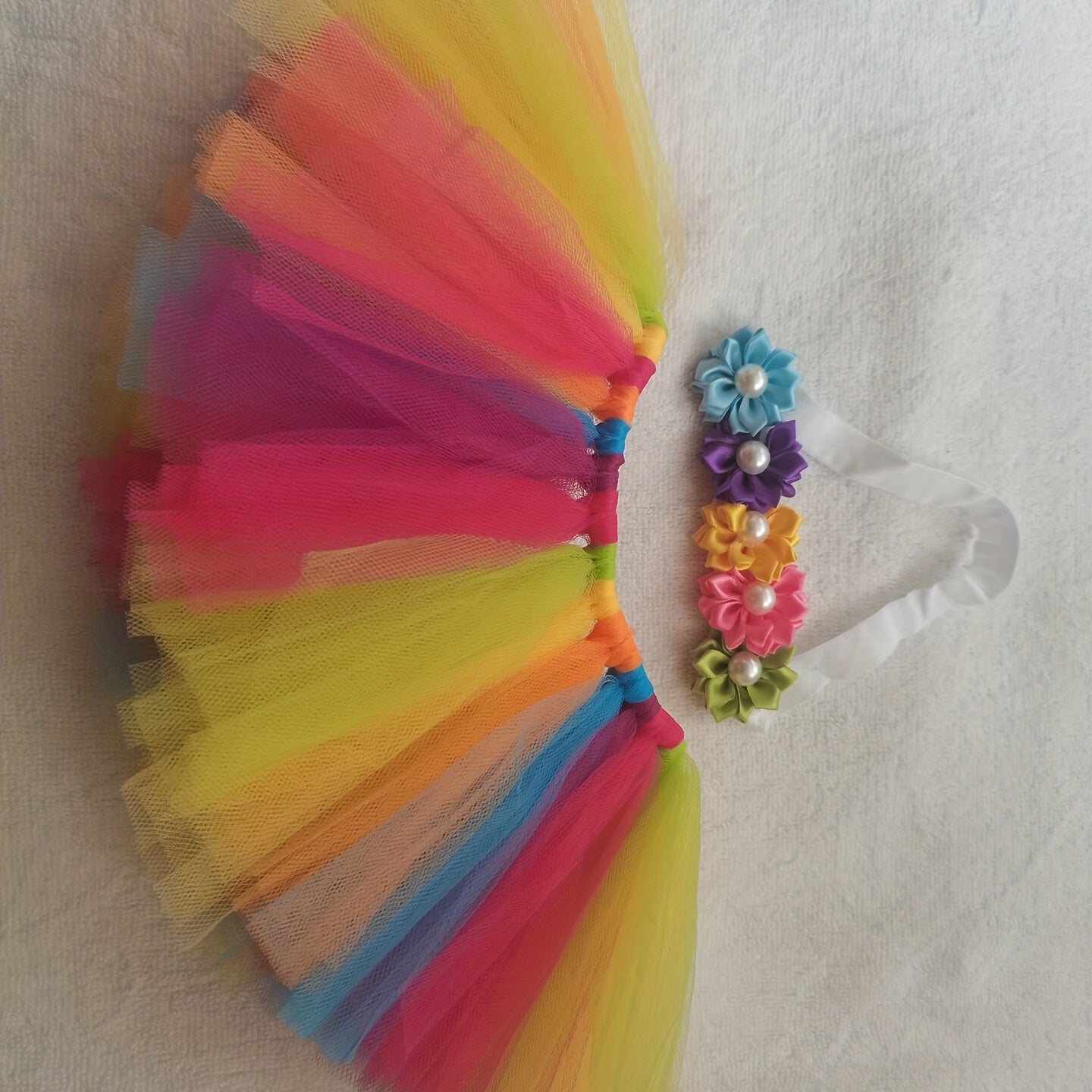 To'plamga Kamalak rangli tutu yubka, qizlar uchun ko'ylak, gullar bilan bezatilgan bosh bant va fotosurat aksessuarlar kiradi.