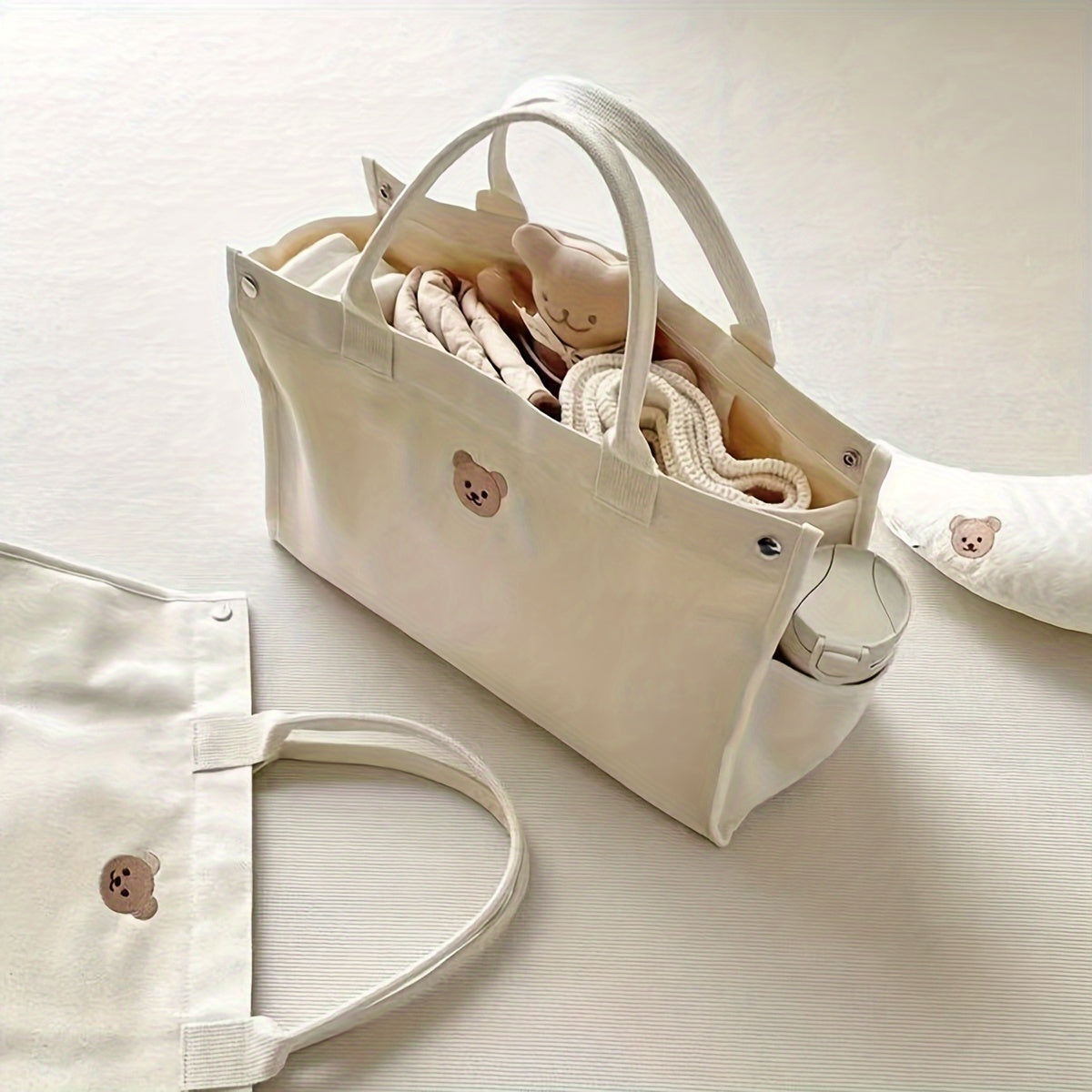 Zarif ayiq mavzusidagi to'plam sumkasi, mustahkam polyesterdan tayyorlangan, tozalash oson va oq rangda, pampers va kundalik zaruriy buyumlarni tashish uchun ideal.