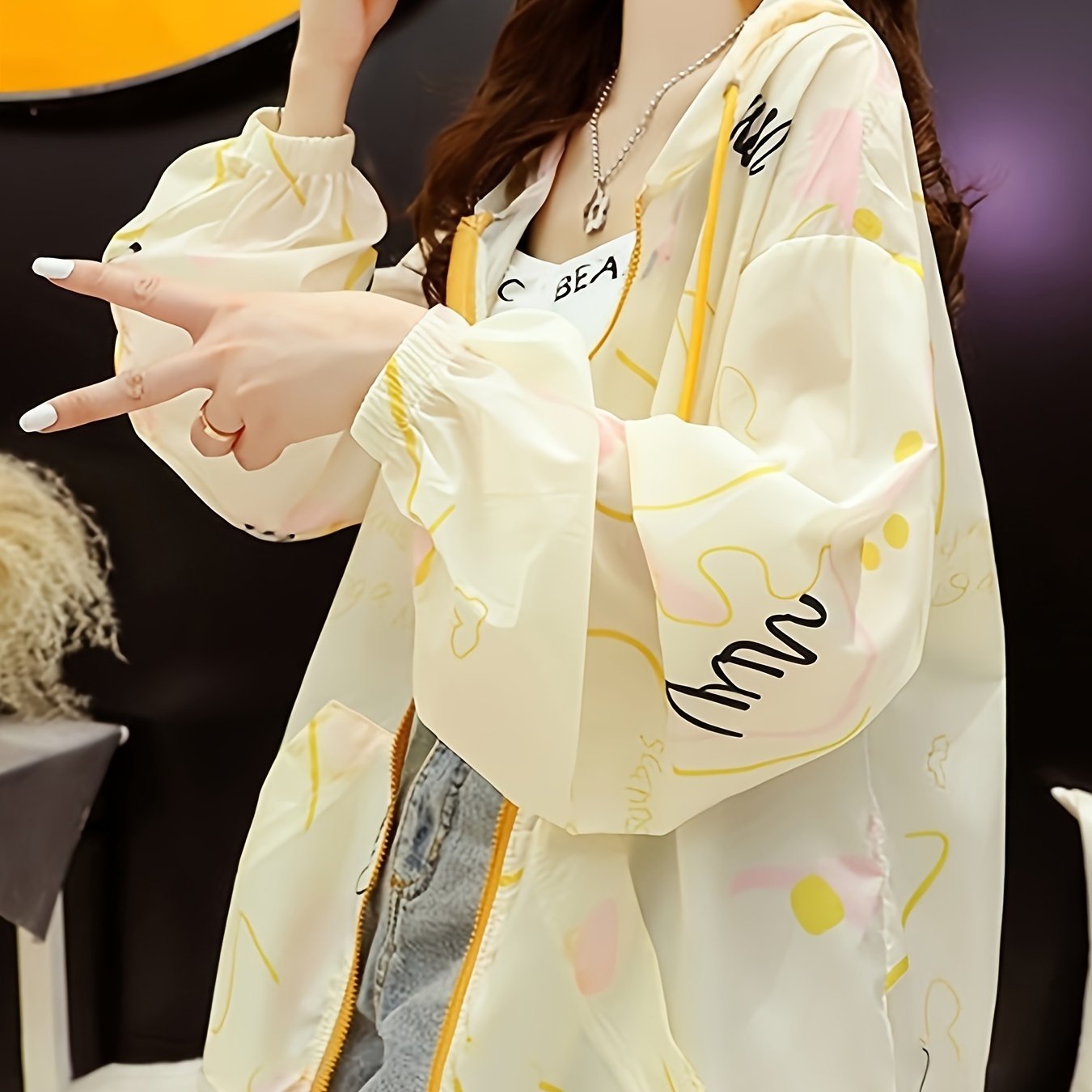 Ayollar uchun oq kaputli jaket, sariq aksentlar bilan va quyoshdan himoya, sport uslubidagi Koreya dizayni bilan chiziqli uzun yenglar bilan. Nafas oladigan polyester aralashmasidan tayyorlangan, bahor uchun mukammal.