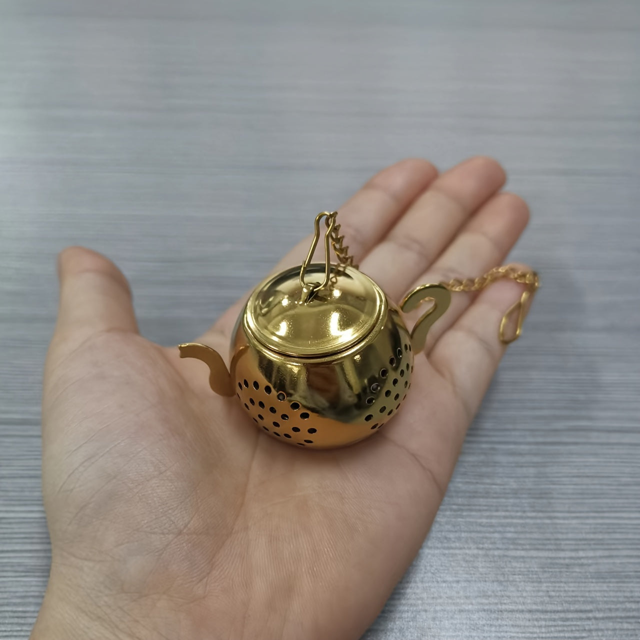 Oltin gul zanglamas po'latdan yasalgan choynak shaklidagi choy filtr, bir xil filtr teshiklari va chashkalar uchun osma zanjir bilan.