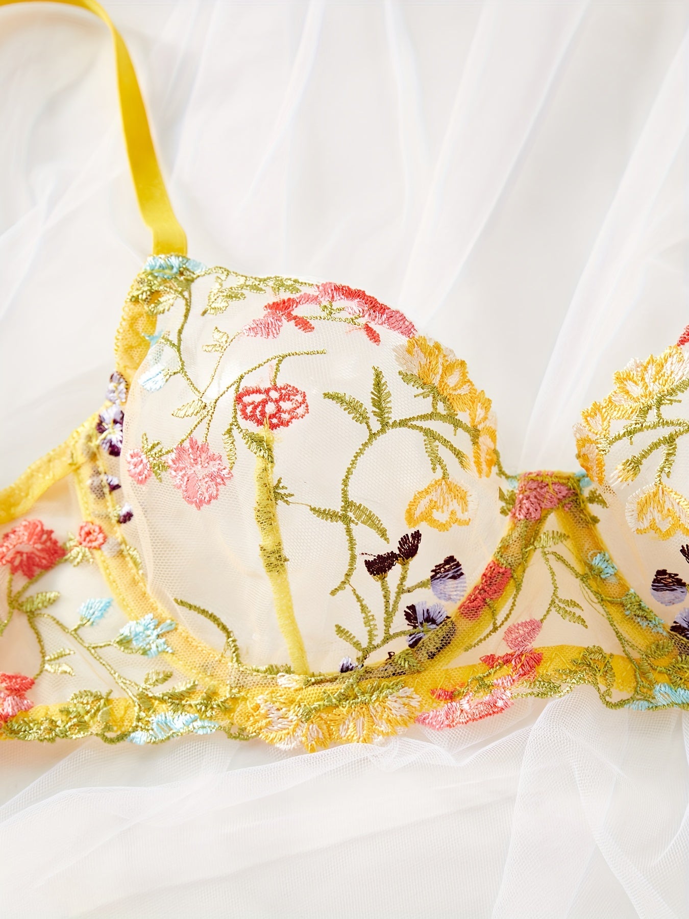 Sariq yarim shaffof to'rli ichki kiyim to'plami, gullar bilan bezatilgan, brassi va thongni o'z ichiga oladi. Zamonaviy va jozibali ko'rinish uchun mukammal.