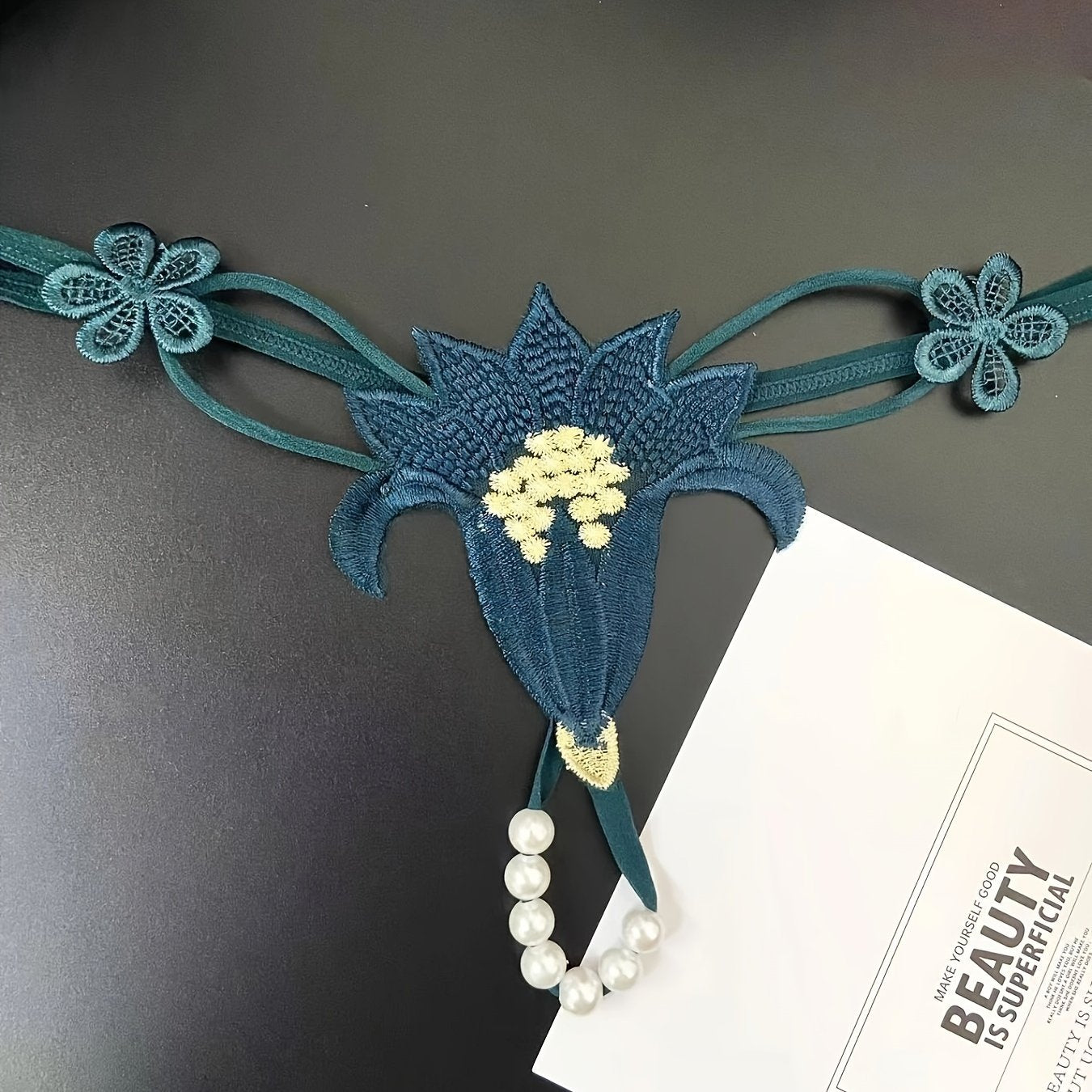 Красный кружевной корсет с перловыми деталями и соответствующим низким стрингом, украшенным цветами крючком и бисерными элементами.