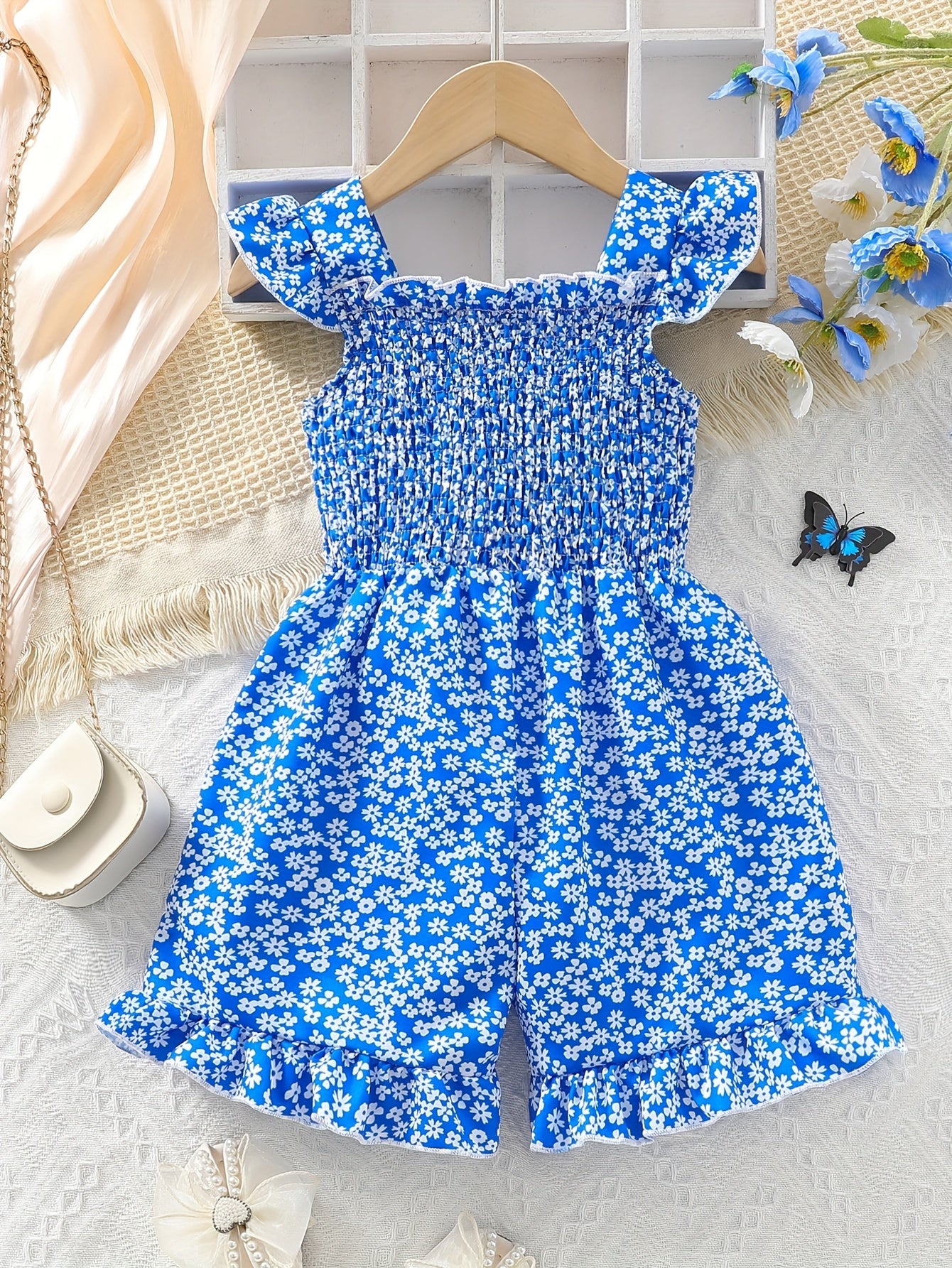 Yoshlar uchun qirqma detali, kamon va gullar printi bilan bezatilgan yengsiz kombinezon. Polyesterdan tayyorlangan, yozgi sayrlar va partiyalar uchun mukammal.